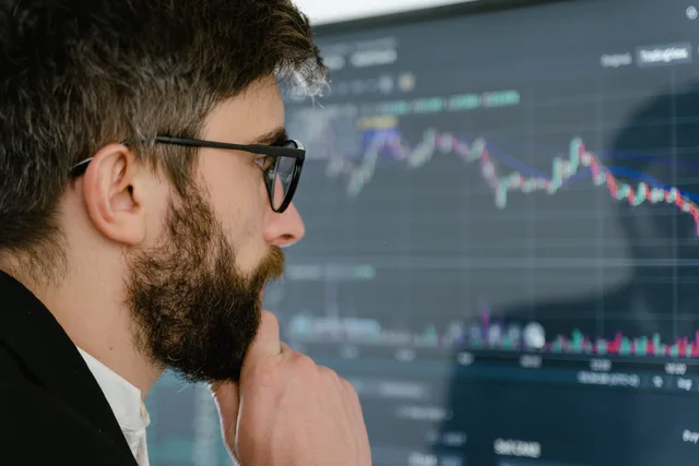 A focused man with glasses studies stock market graphs on a screen, pondering insights. Schweizer Konjunktur verstehen: BIP, Wachstum und Datenquellen
